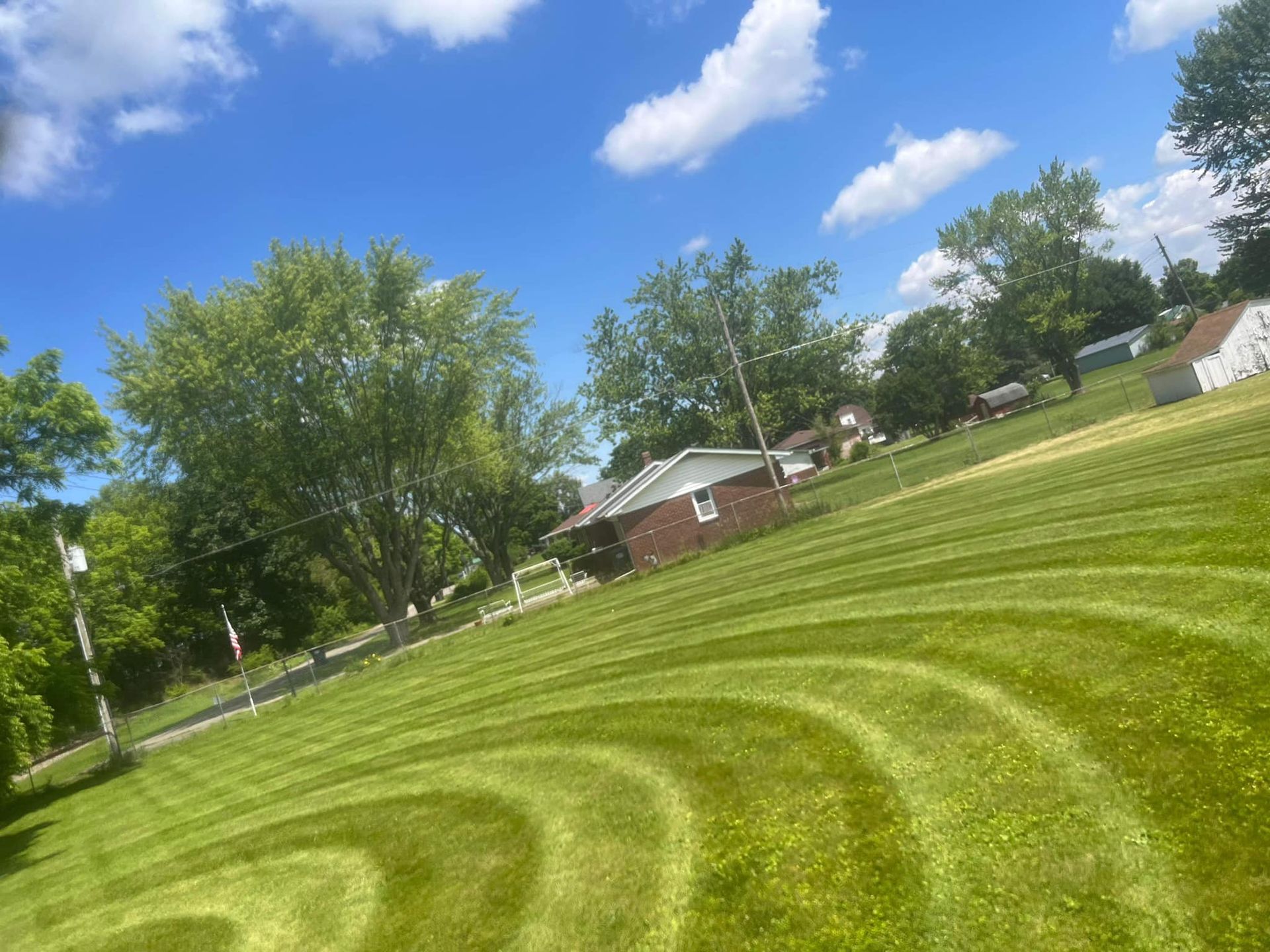 A lush green lawn with a house in the background and trees in the foreground.