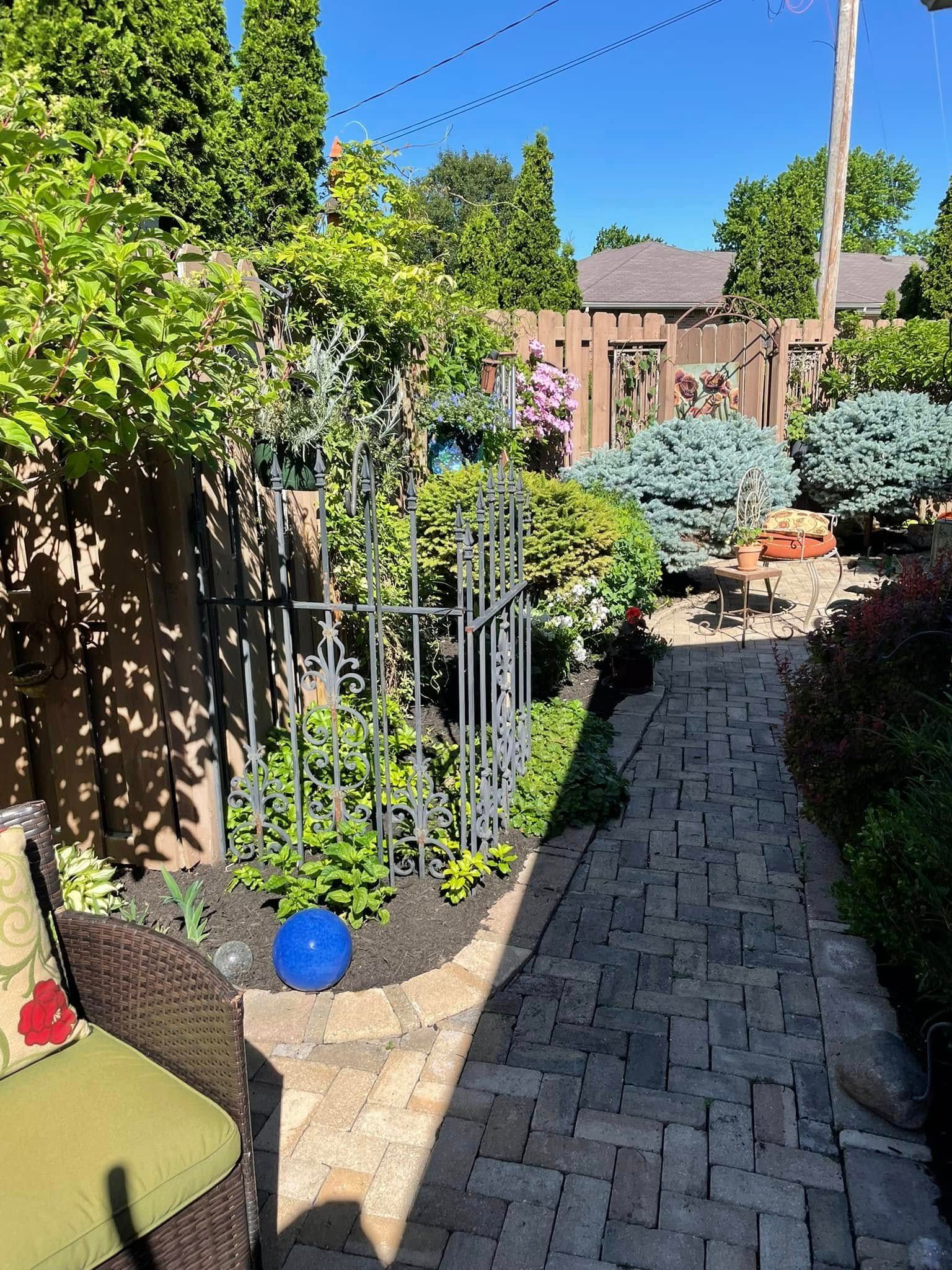 A brick walkway leading to a patio with a wicker chair and a blue potted plant.
