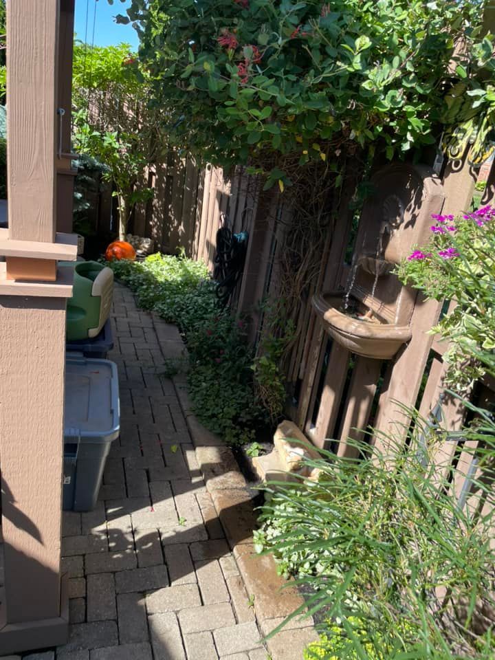 A brick walkway leading to a wooden fence surrounded by plants and flowers.