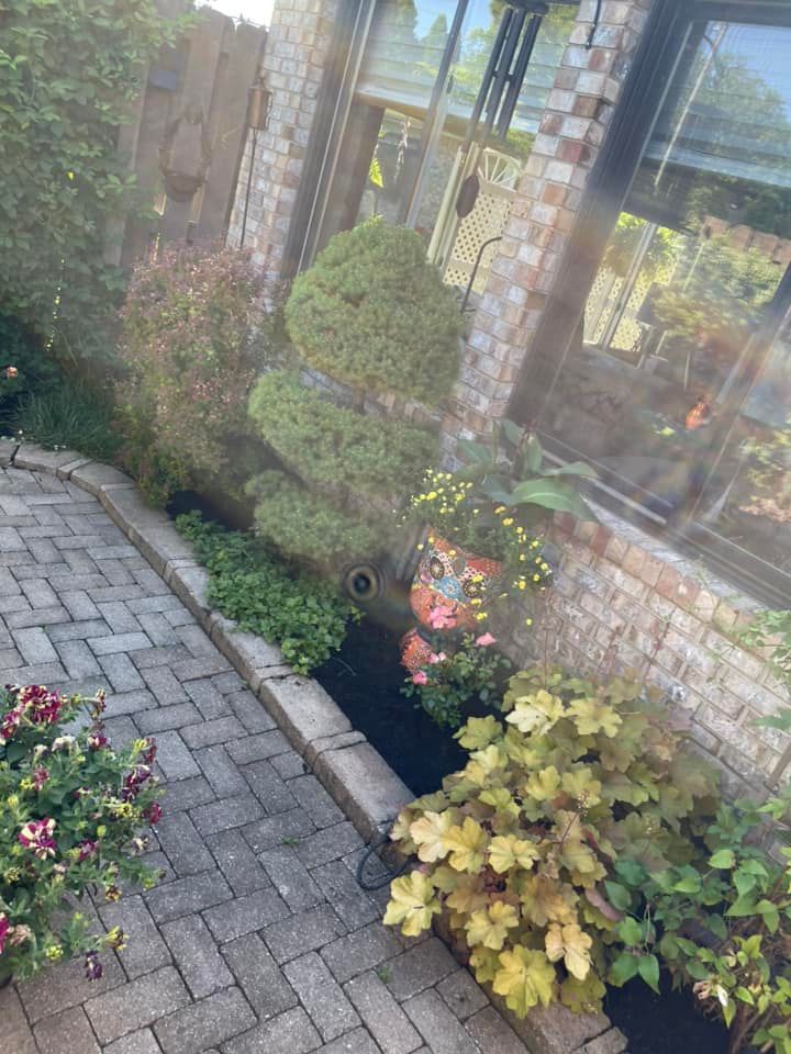 A brick walkway leading to a house with lots of plants and flowers.