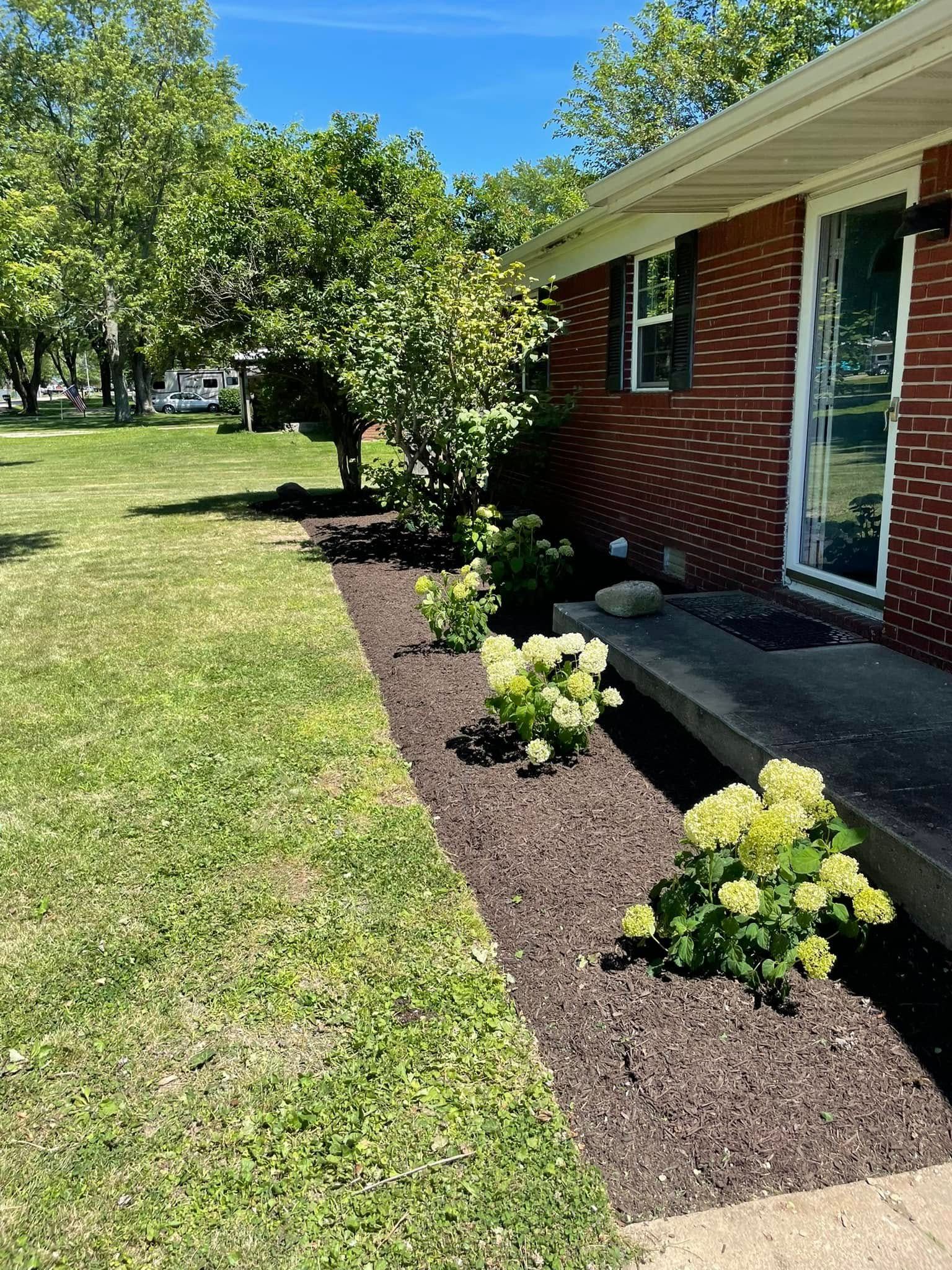 A brick house with a lush green lawn and flowers in front of it.