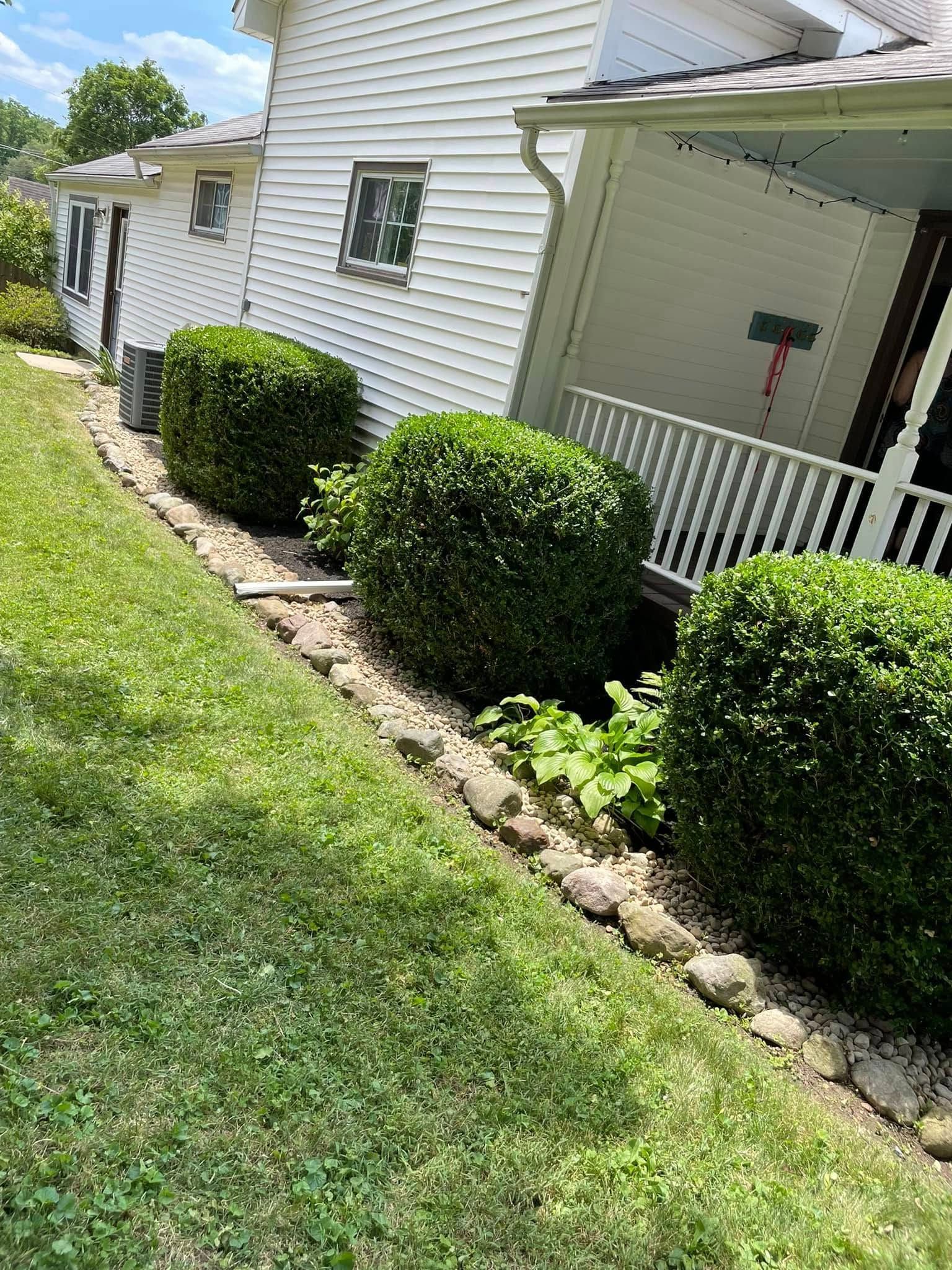A white house with a porch and bushes in front of it.