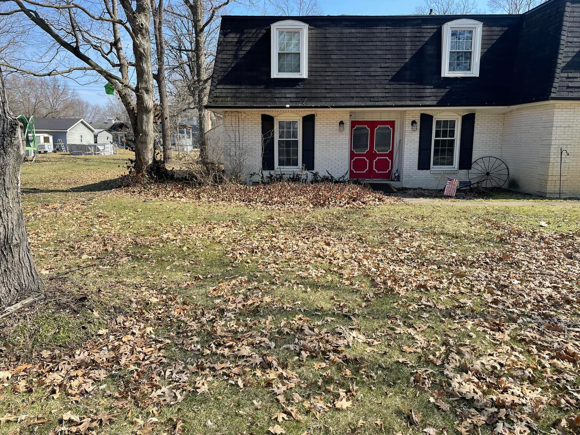 A white house with a red door and black shutters is sitting on top of a lush green field.