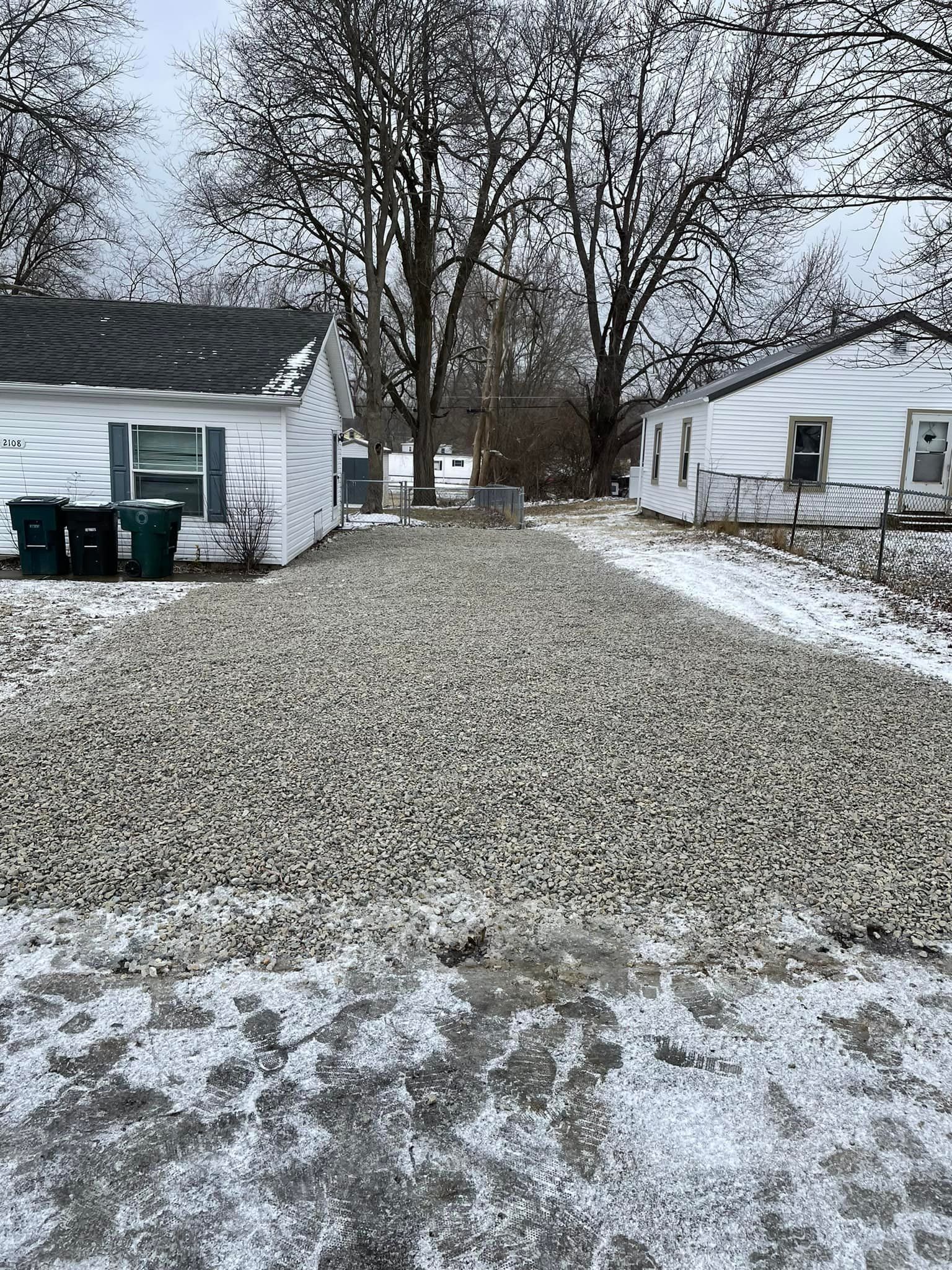 A gravel driveway leading to a house in the snow.