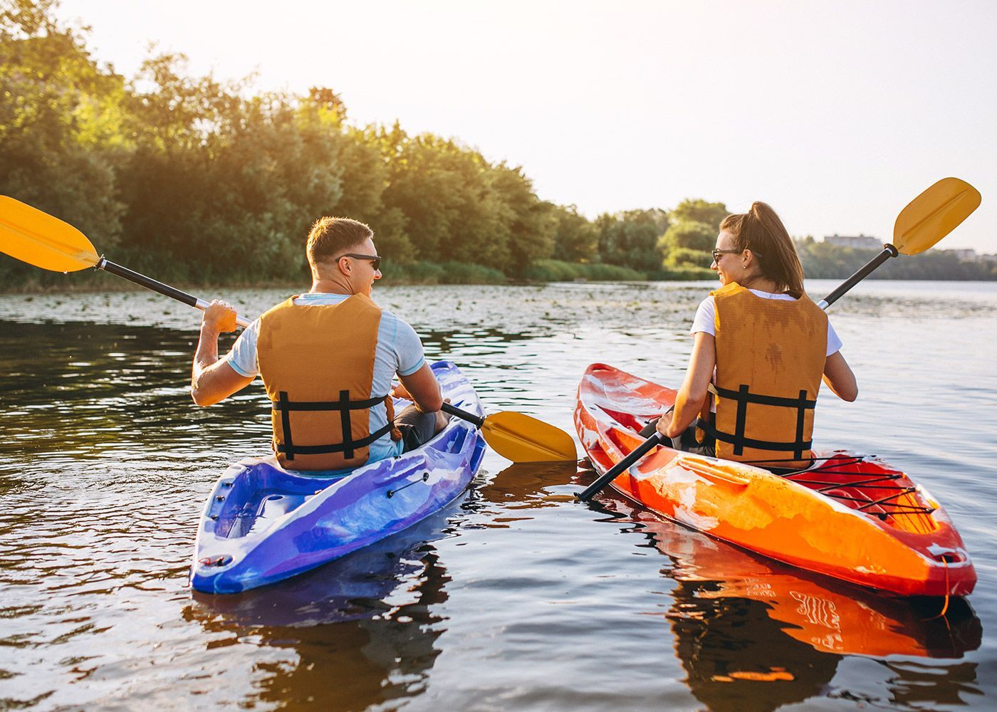 A man and a woman are paddling kayaks on a lake.