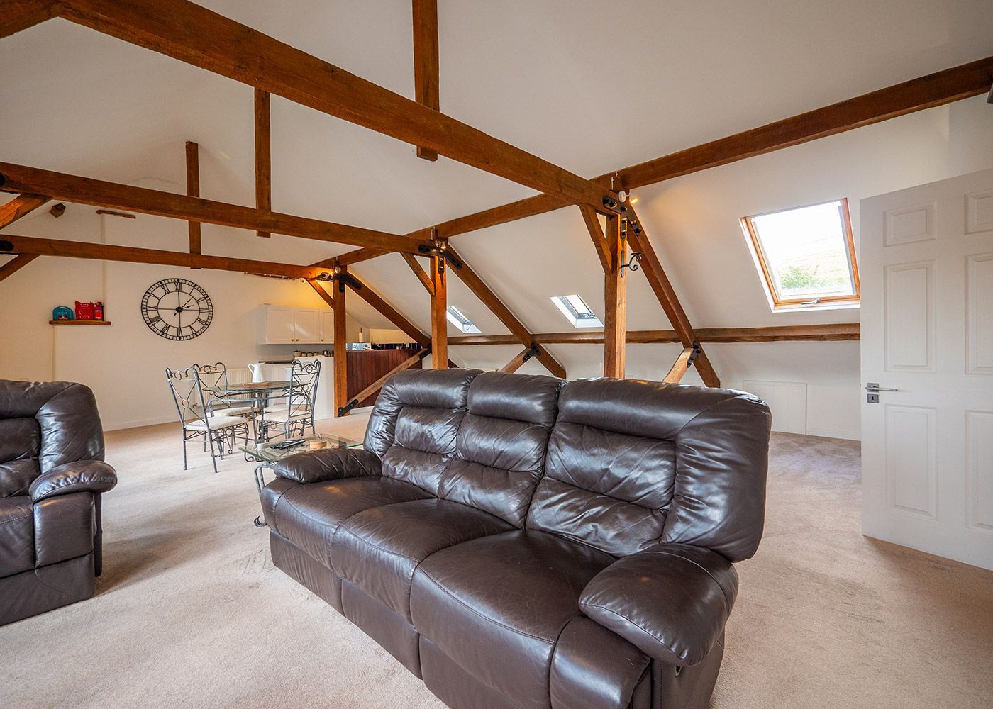 A living room with a brown leather couch and a clock on the wall.