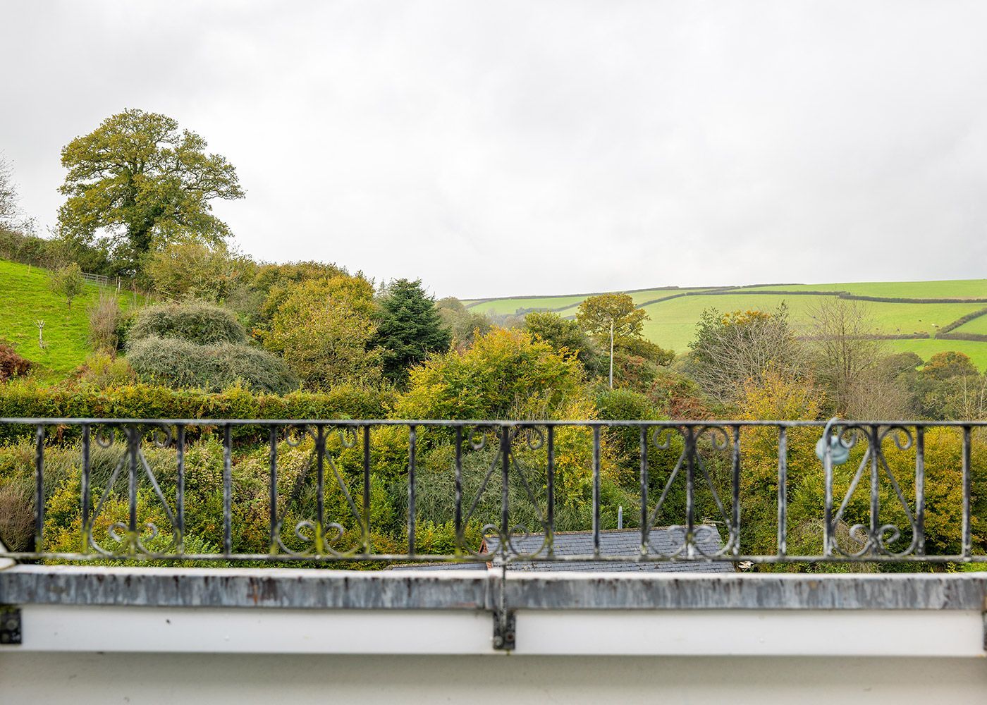 A balcony with a view of a lush green field and trees.