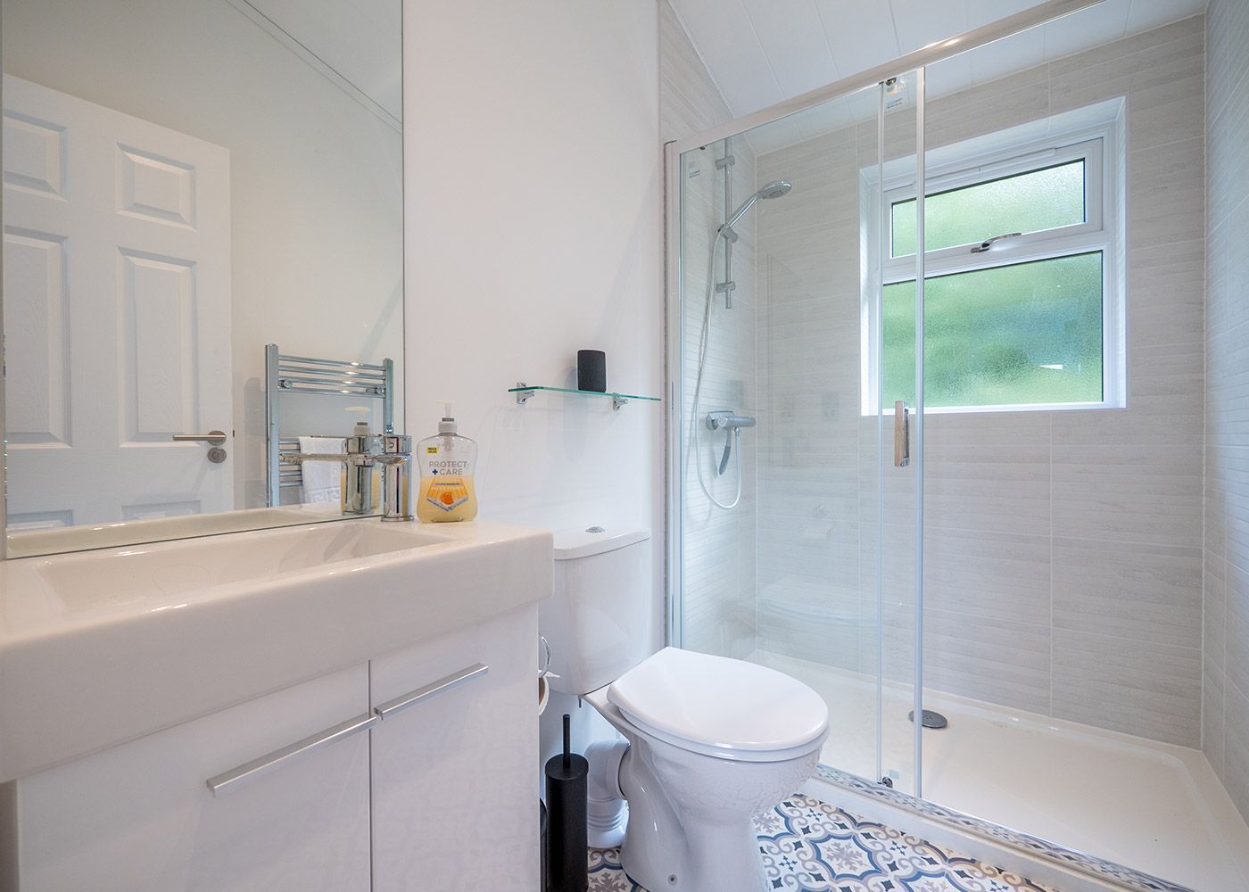 A bathroom with a toilet , sink , mirror and walk in shower.