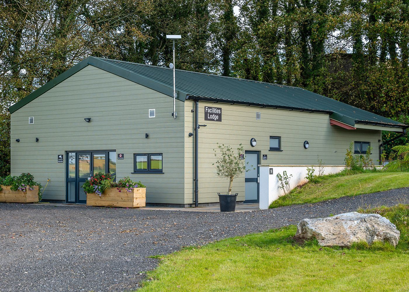 A green building with a green roof is surrounded by grass and trees.