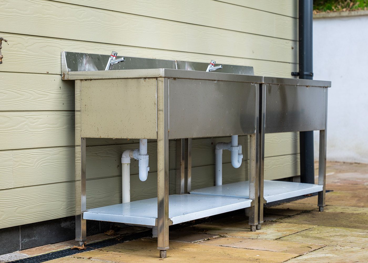 Two stainless steel sinks are sitting outside of a building.