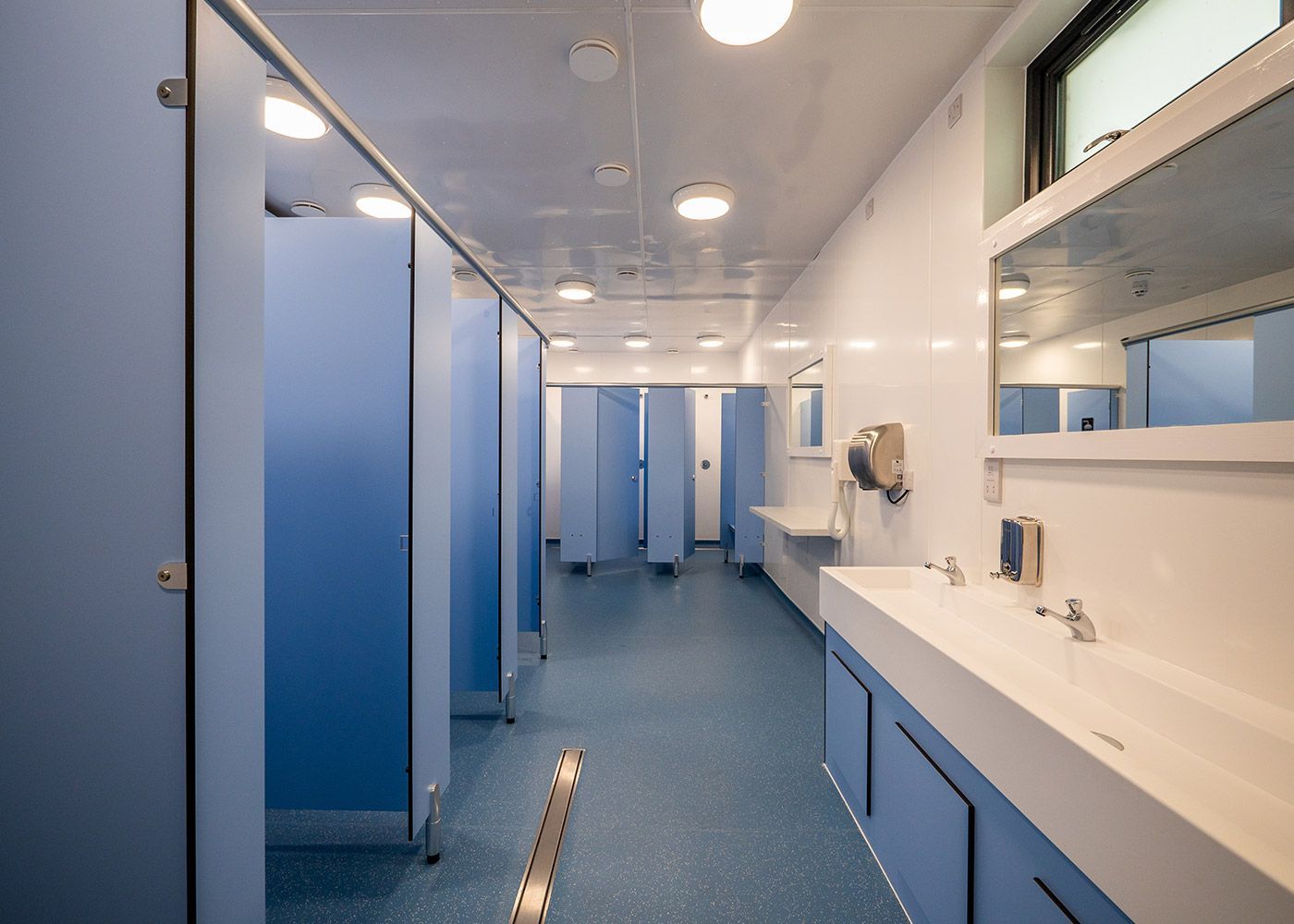A bathroom with blue cubicles and a sink.