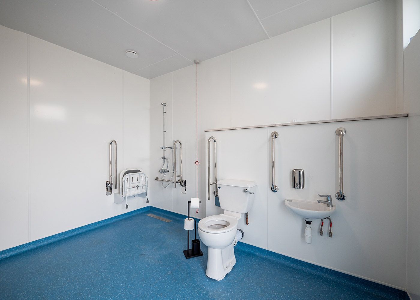 A handicapped bathroom with a toilet , sink and handrails.