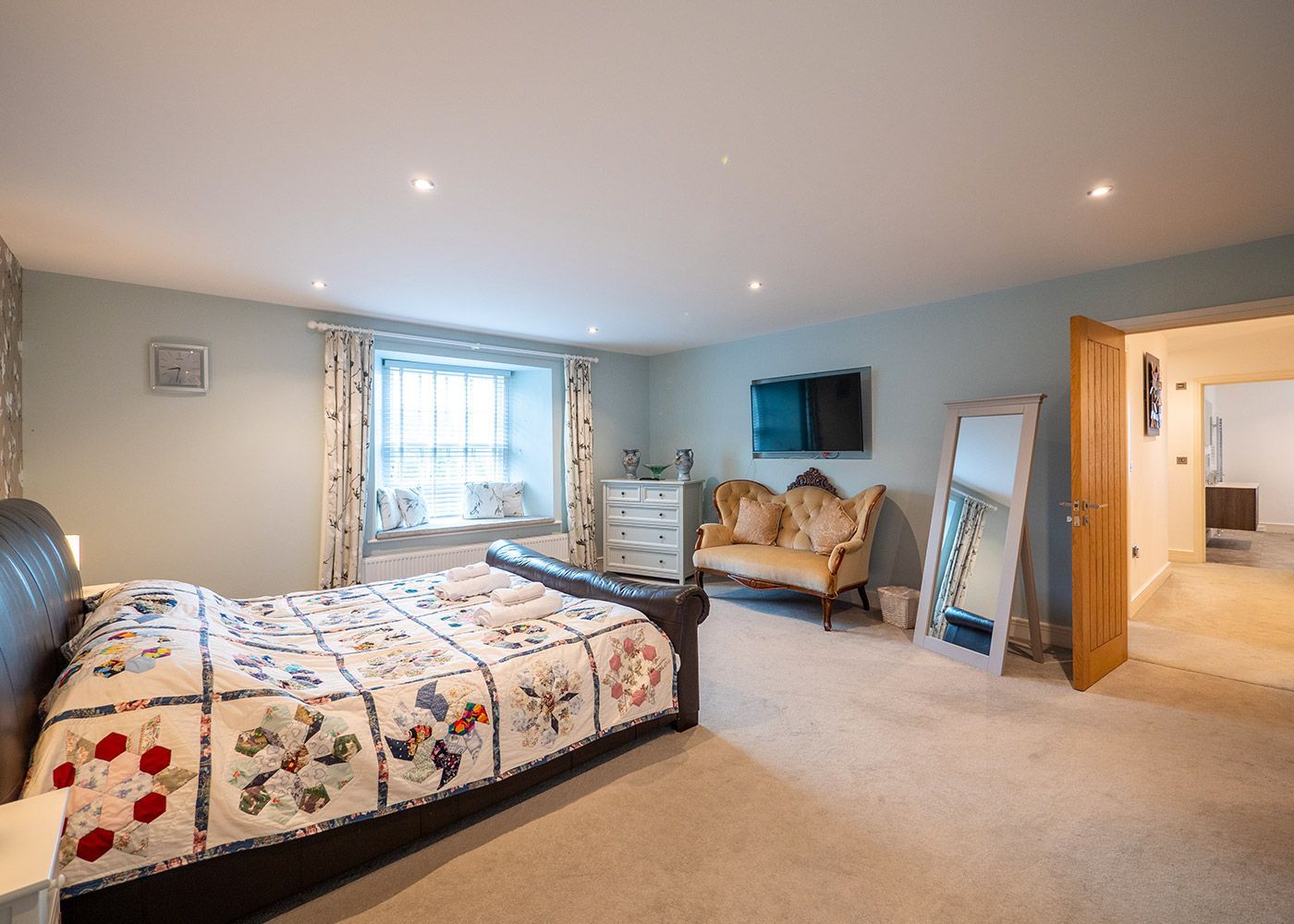 A bedroom with a large bed , couch , dresser and television.