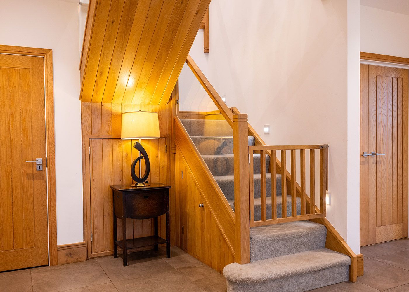A wooden staircase with a lamp on a table in a hallway.