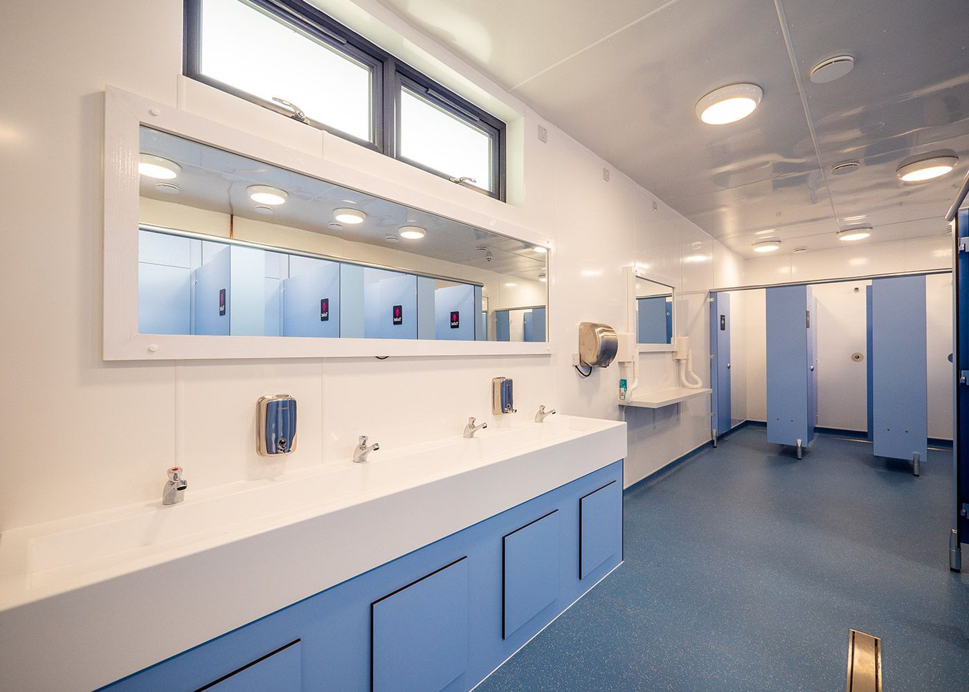 A bathroom with blue cabinets , sinks , mirrors and blue floors.