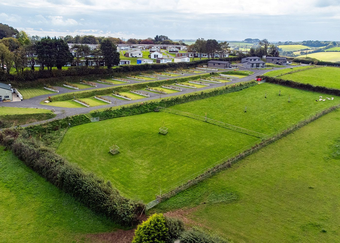 An aerial view of a lush green field with a parking lot in the background.