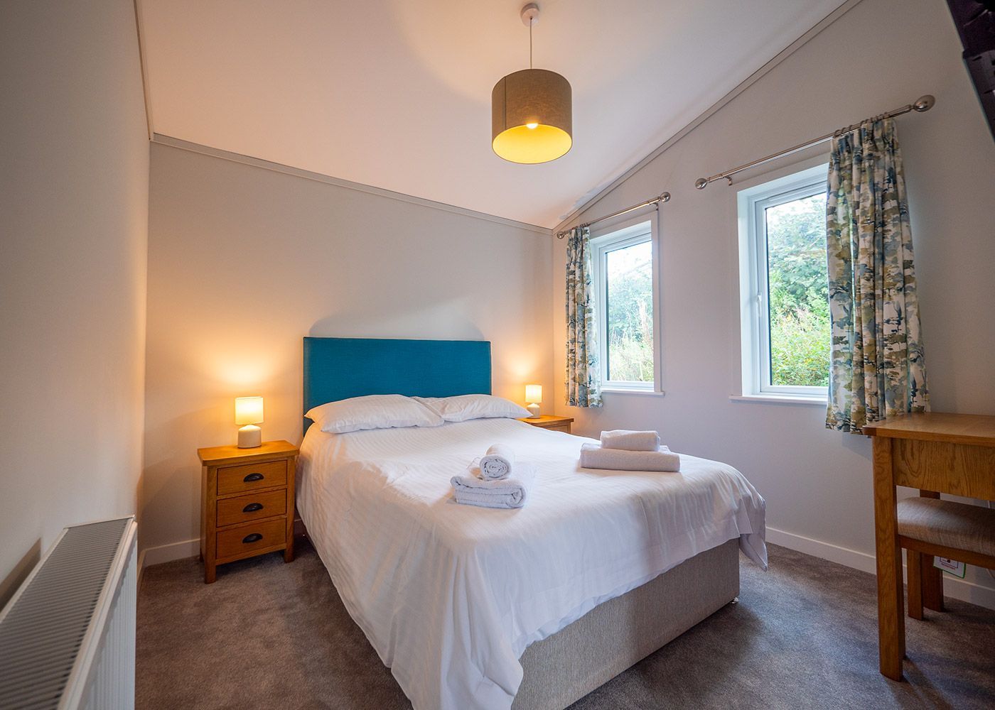 A bedroom with a king size bed , two nightstands , a desk and two windows.