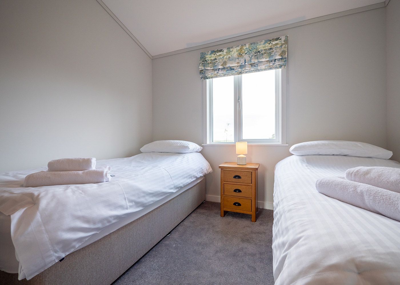 A bedroom with two beds , a nightstand and a window.