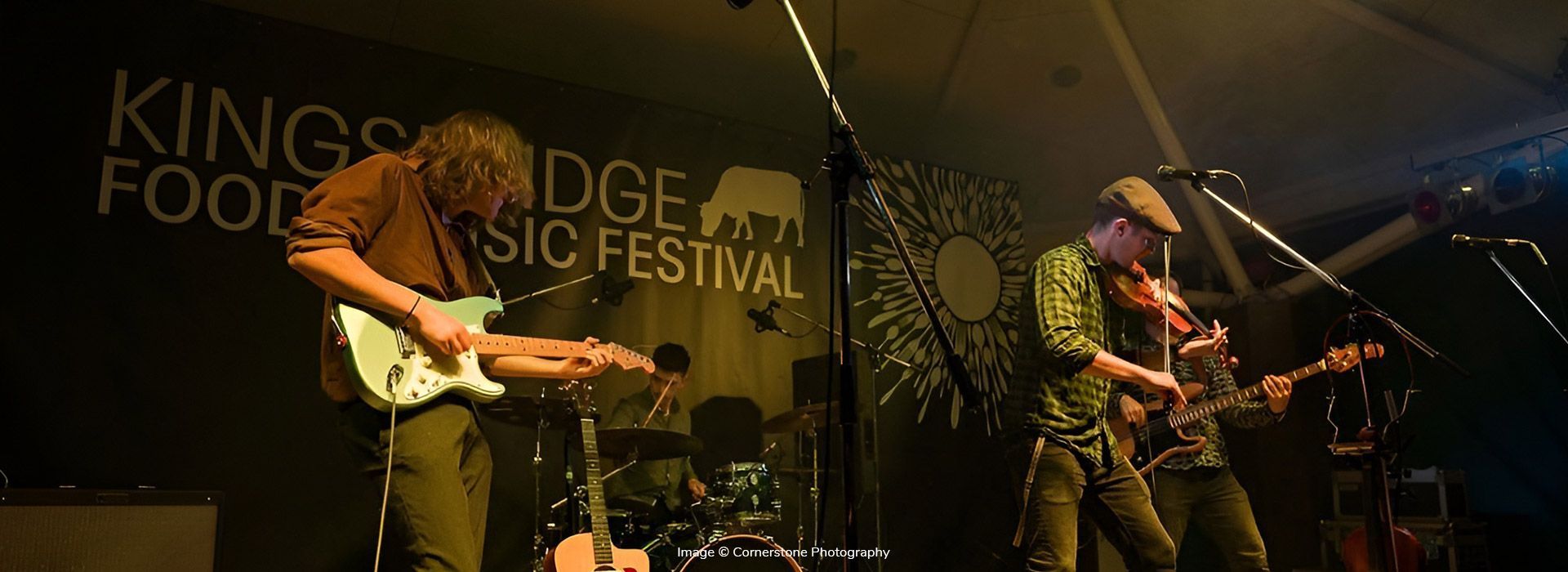 A group of people are playing instruments on a stage at kingsbridge music festival.