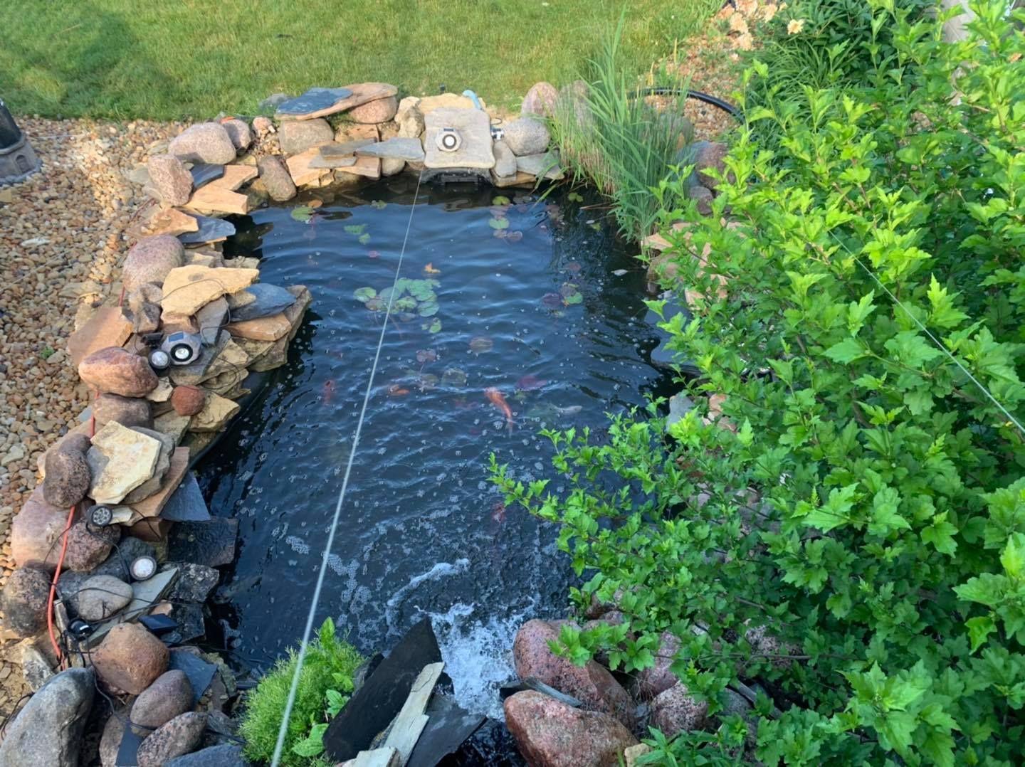 A rectangular stone-lined pond with koi fish, a small waterfall, and surrounding greenery.