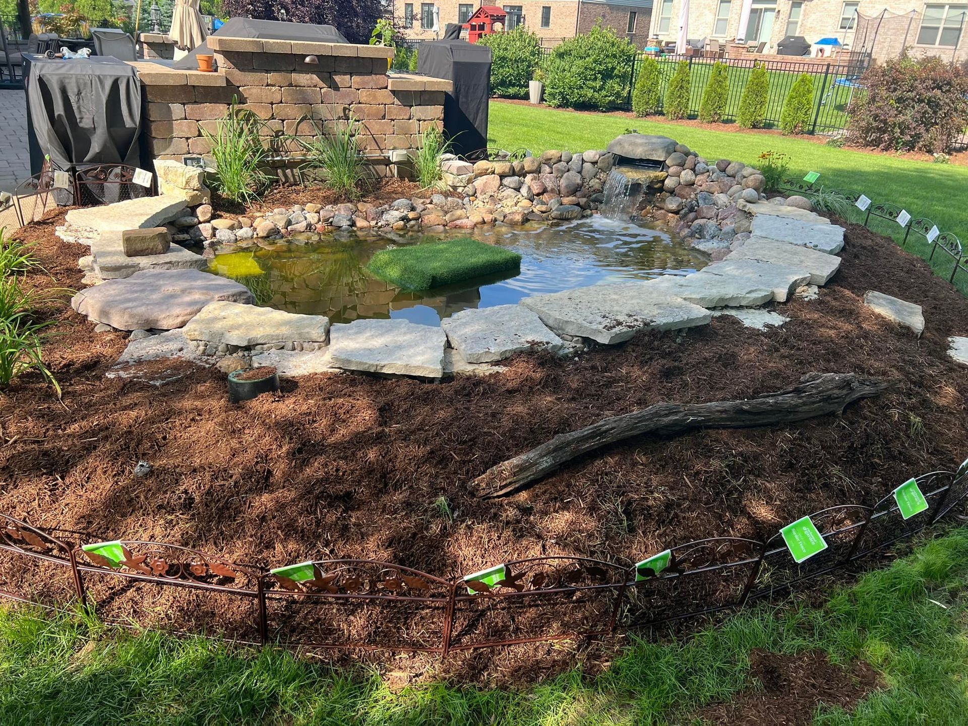 A small pond surrounded by rocks and mulch in a yard.