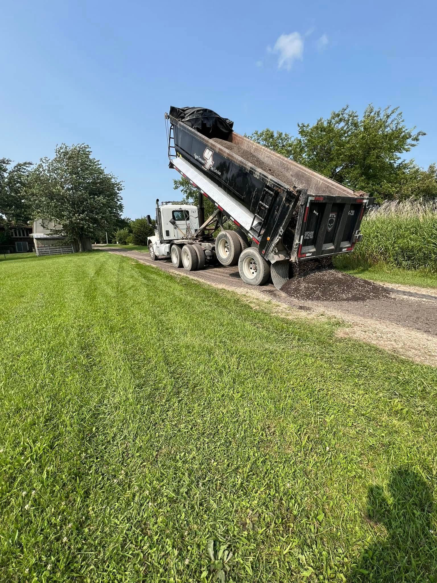 A dump truck is driving down a dirt road in a grassy field.