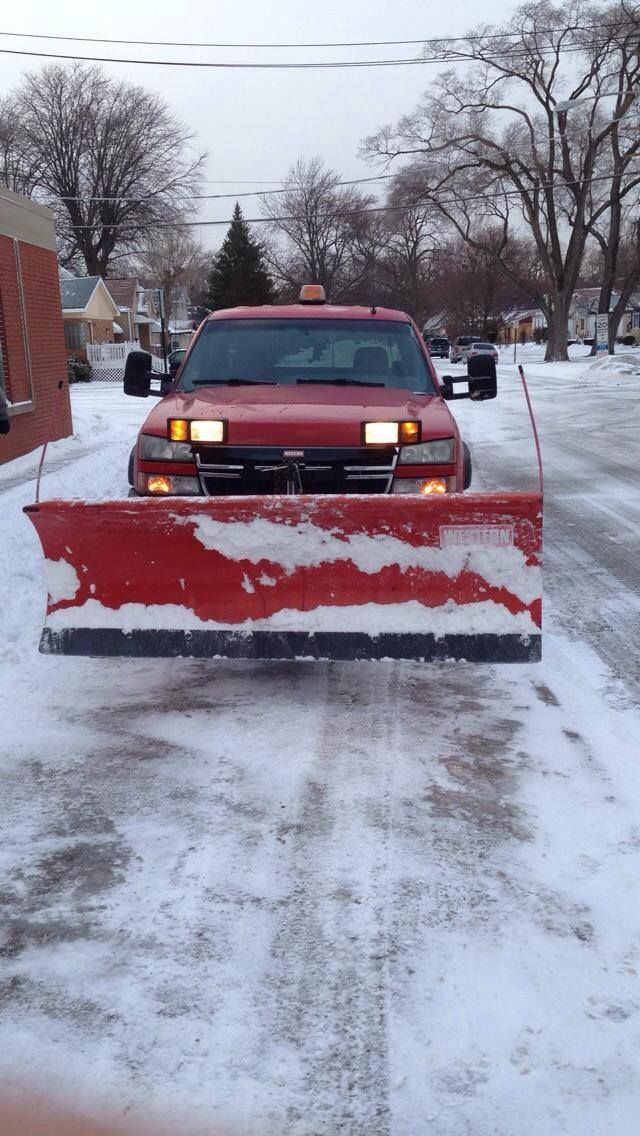 A red snow plow is driving down a snowy street