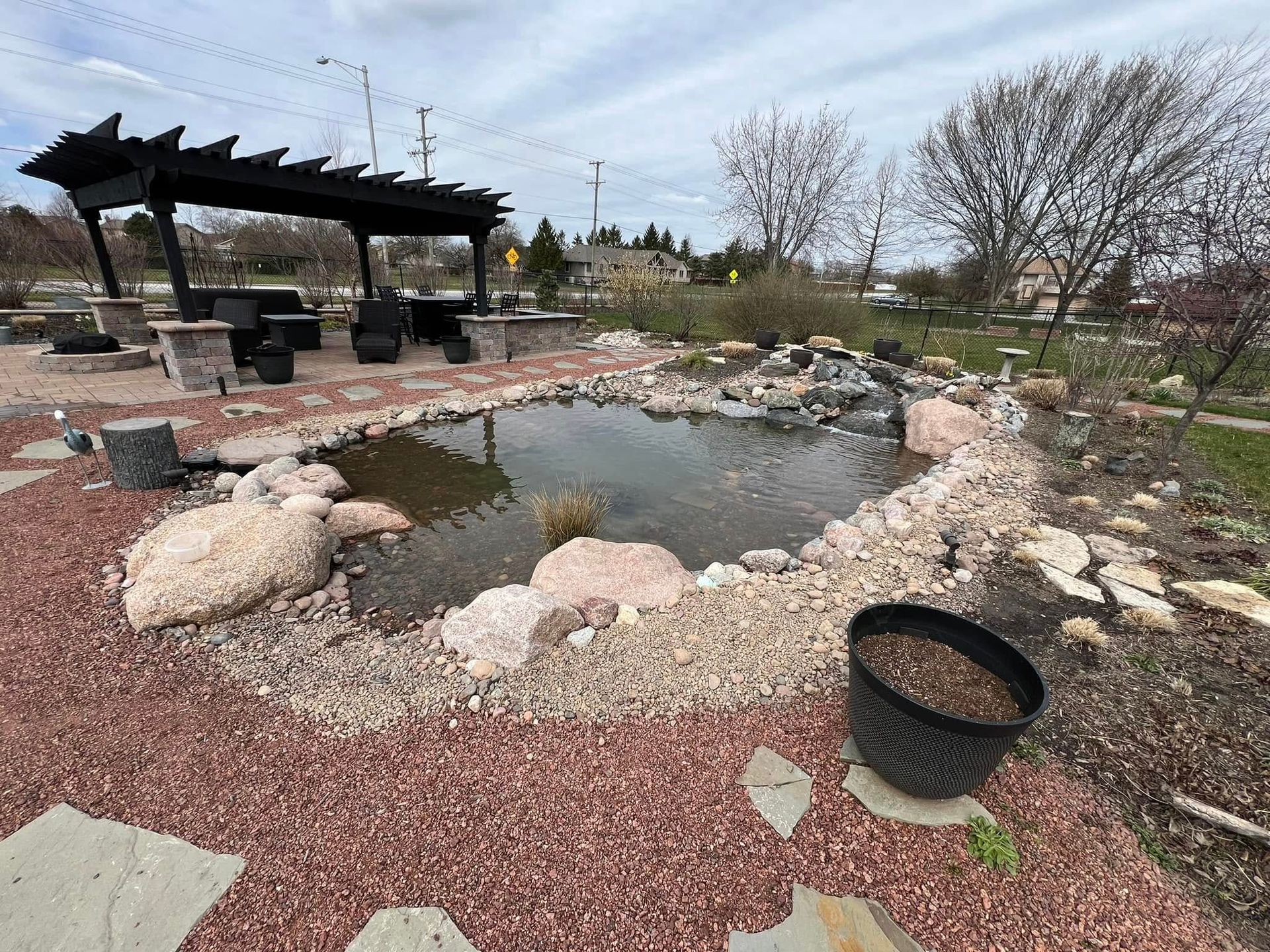 A pond surrounded by rocks and gravel with a pergola in the background.