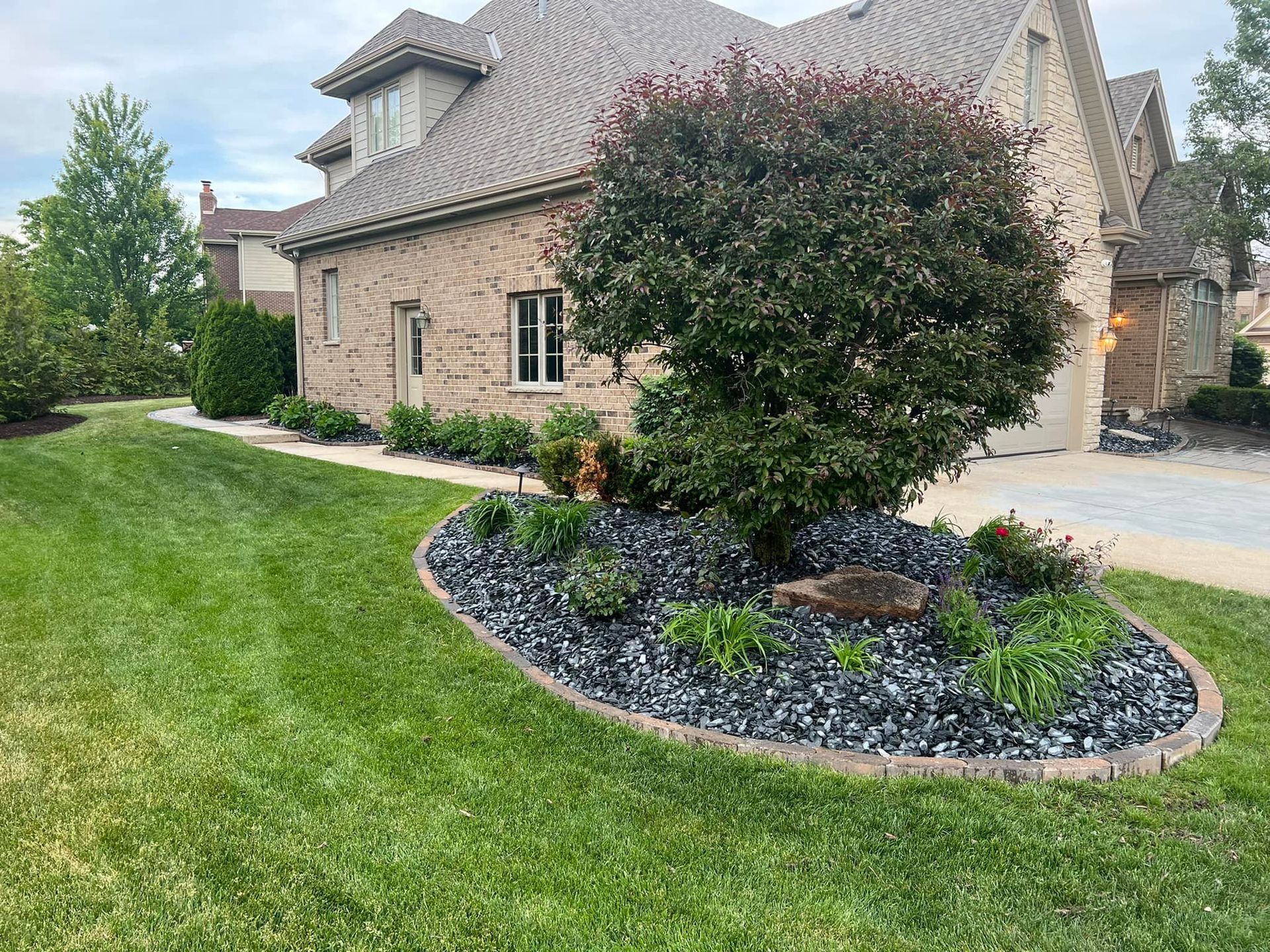 A large brick house with a lush green lawn and a garden in front of it.