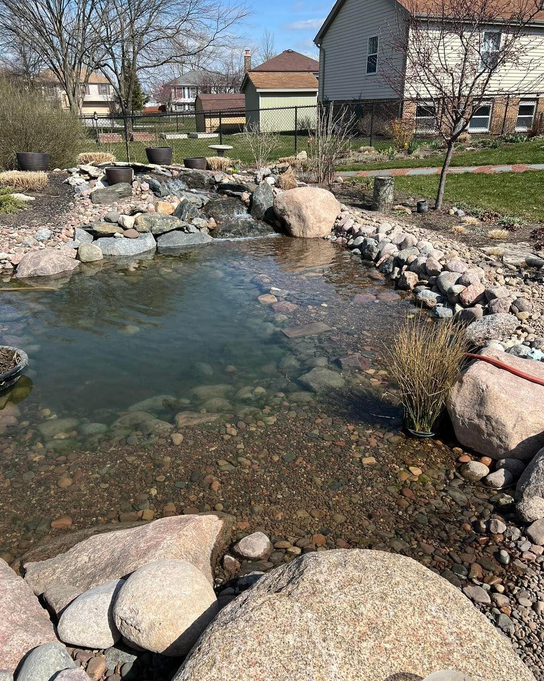 A pond surrounded by rocks and a house in the background.