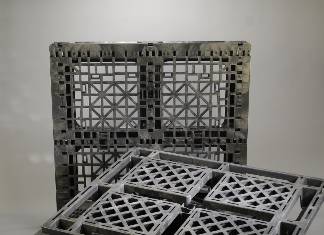 Pile of black and blue plastic pallets against a white backdrop, lit by studio lights.