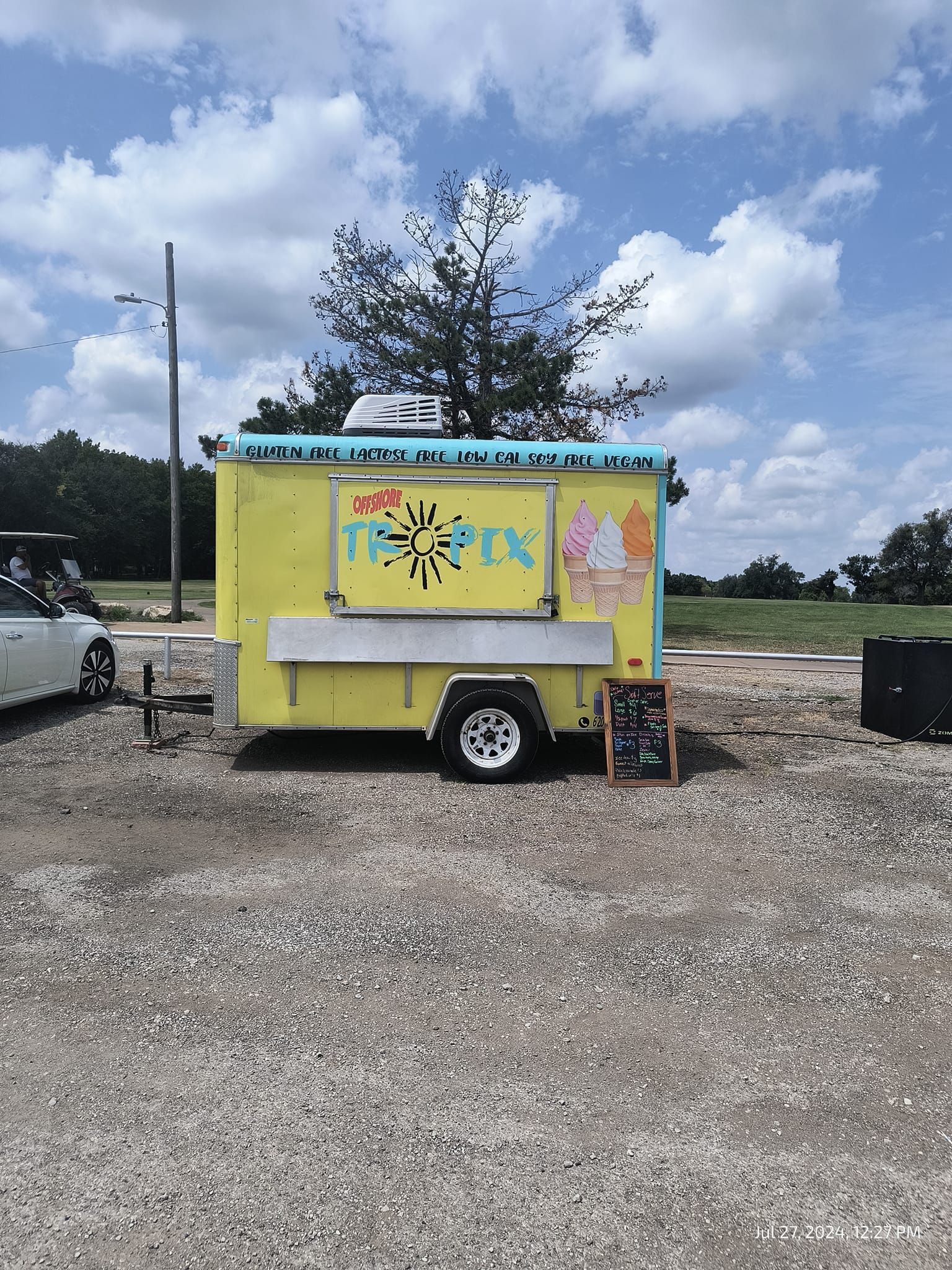 A yellow and blue food truck is parked in a gravel lot.