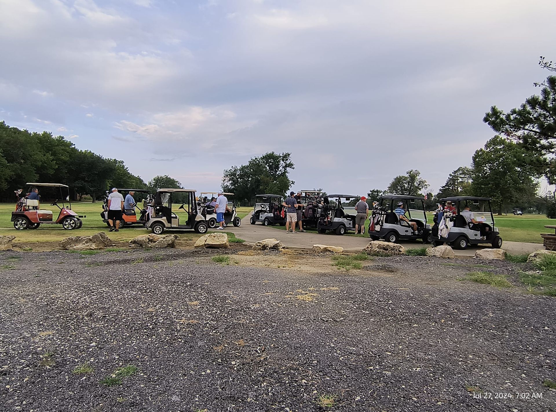 A group of golf carts are parked in a gravel lot.