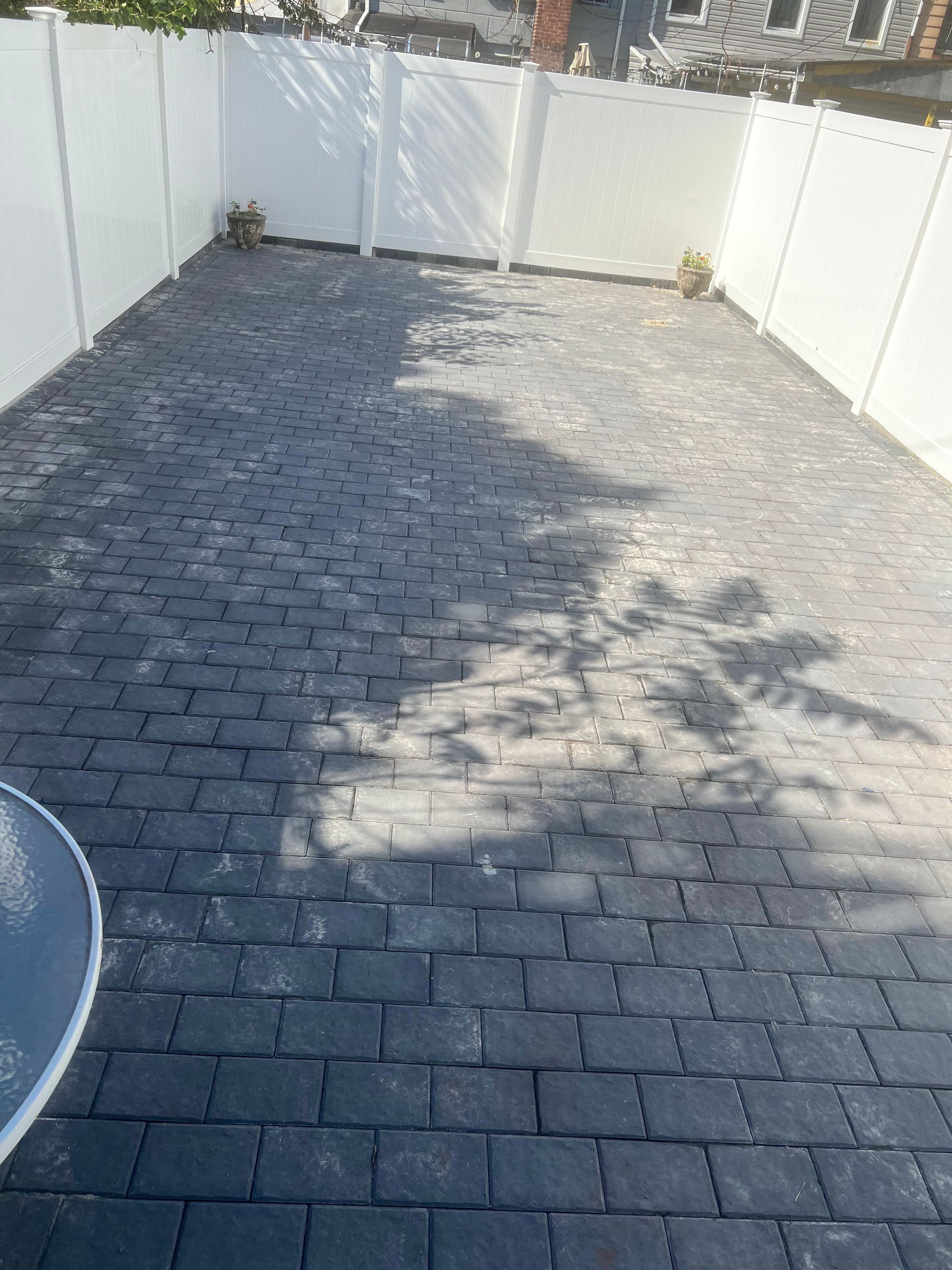 A brick driveway with a white fence in the background.