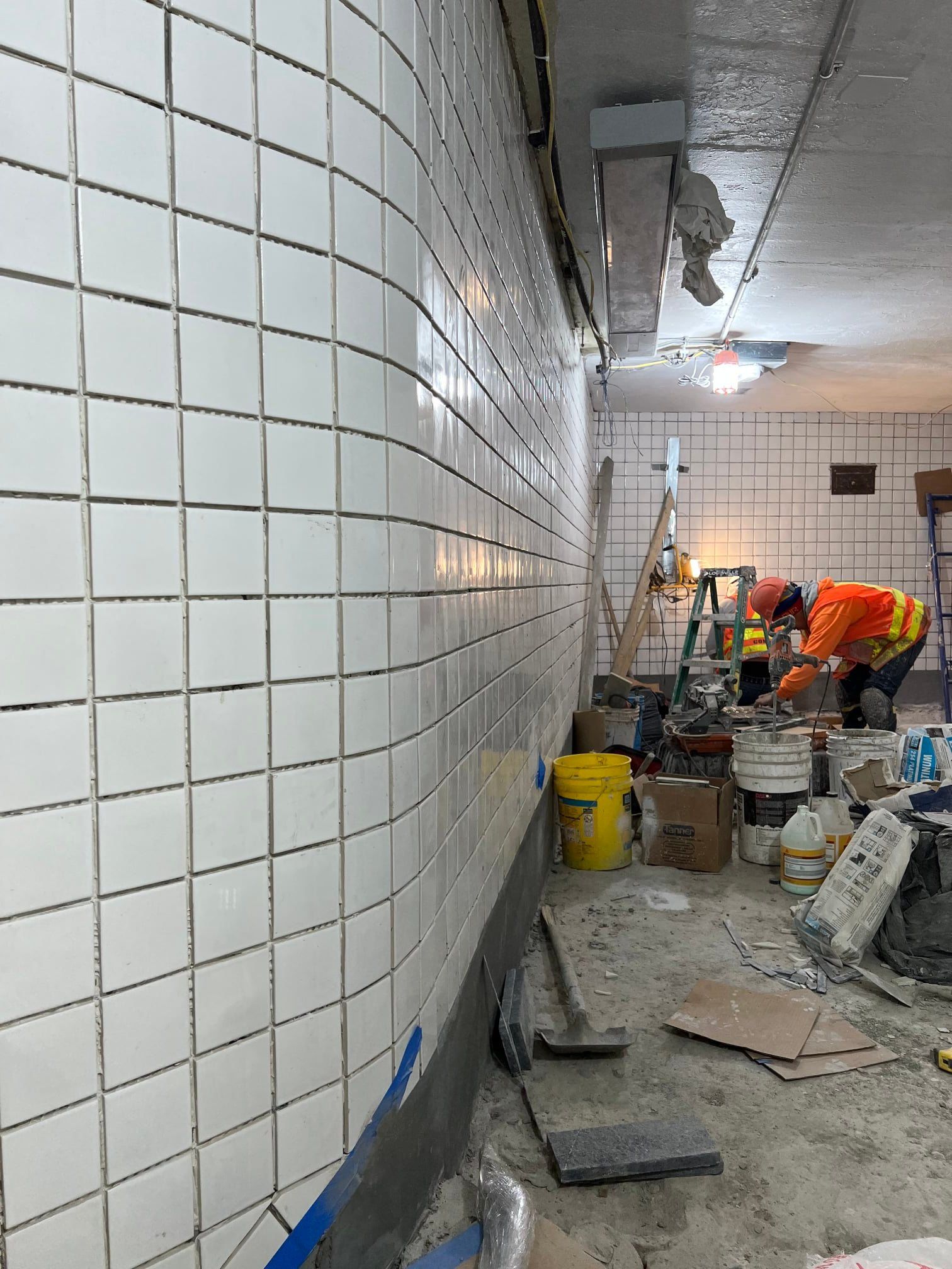 A man is working on a wall in a room with white tiles.