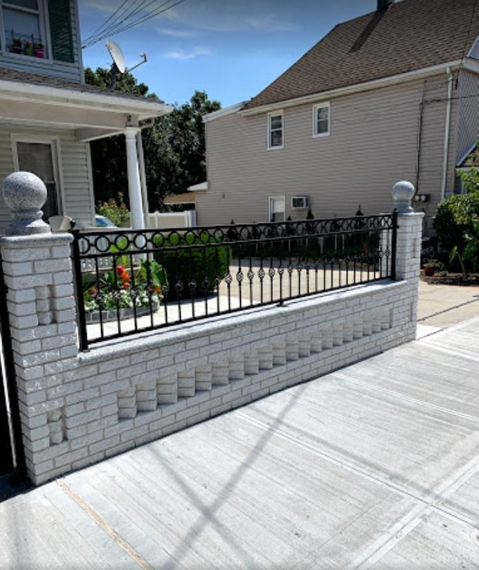 A white brick wall with a black railing in front of a house