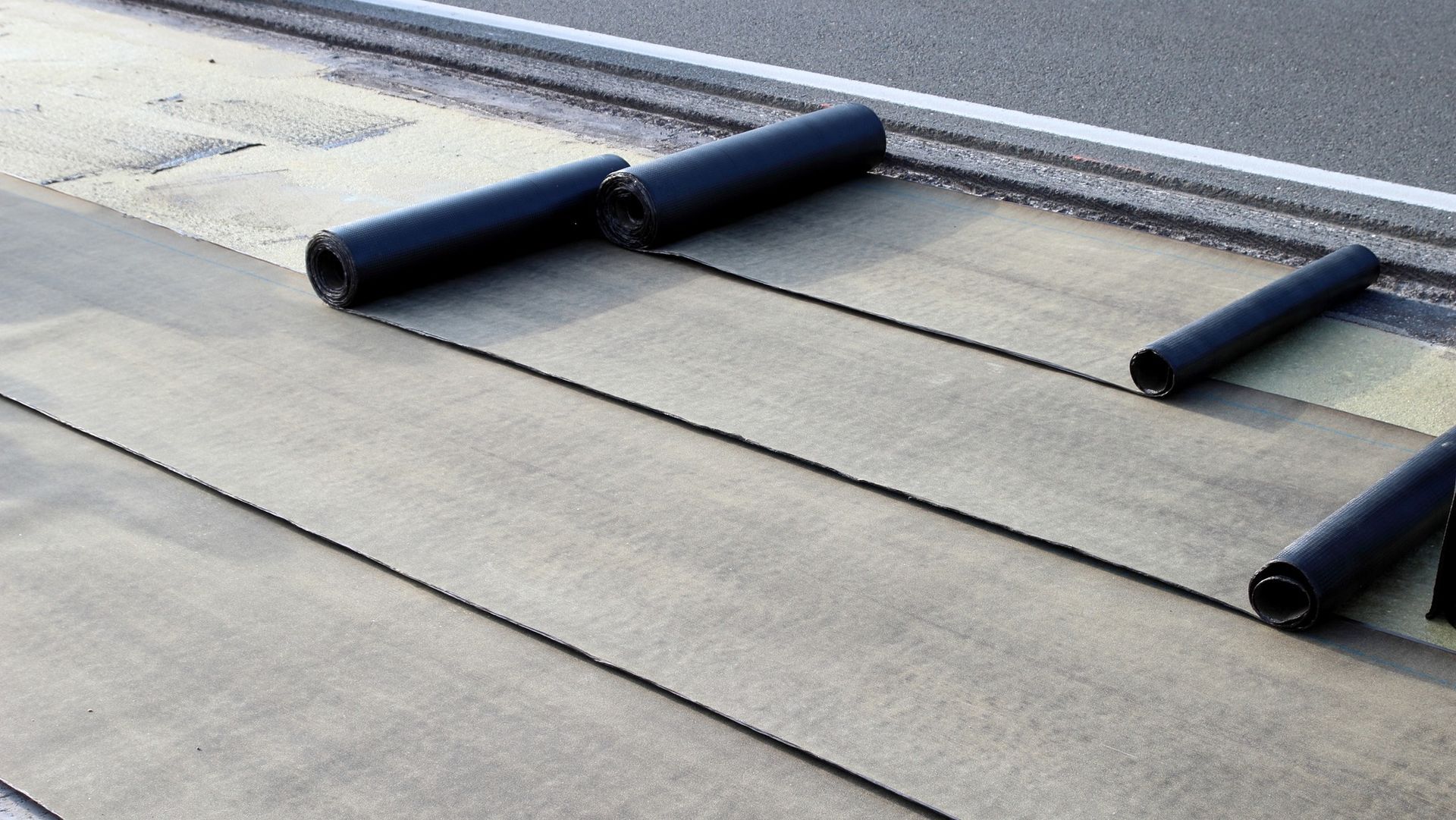Rolls of asphalt are being rolled on a concrete surface.