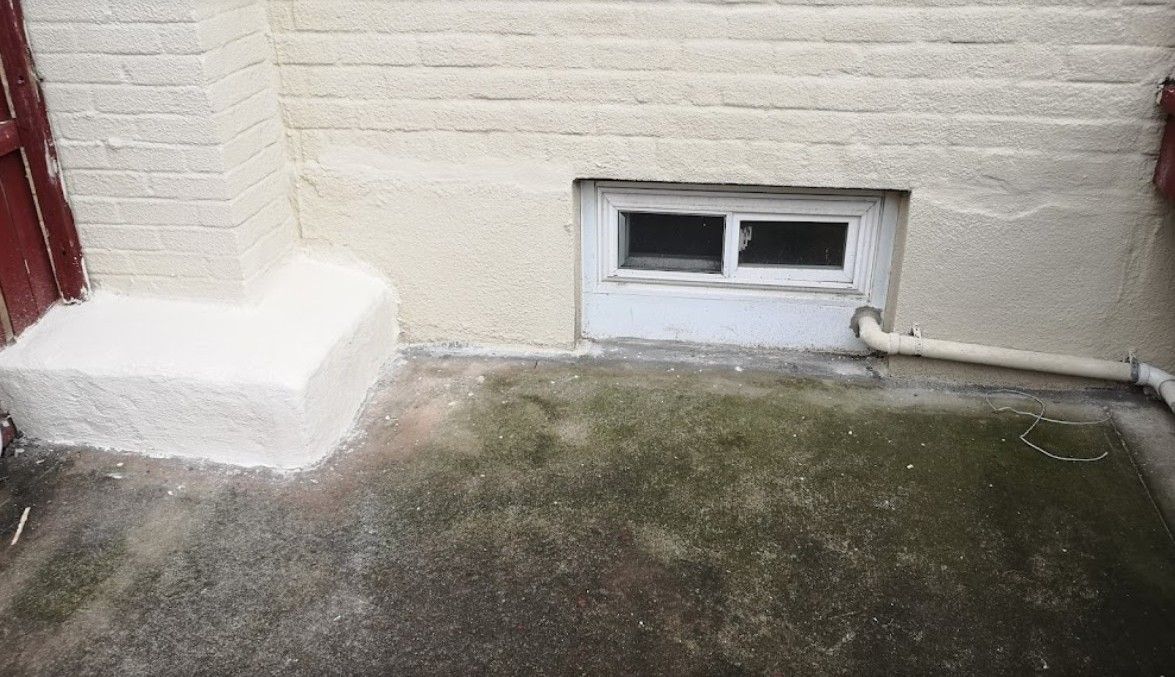 A brick wall with a window and a drain on the side of it.