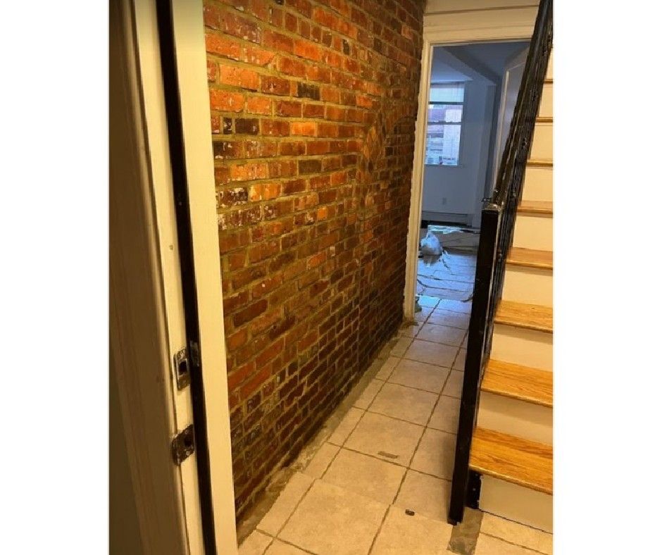 A hallway with a brick wall and stairs leading to a room.