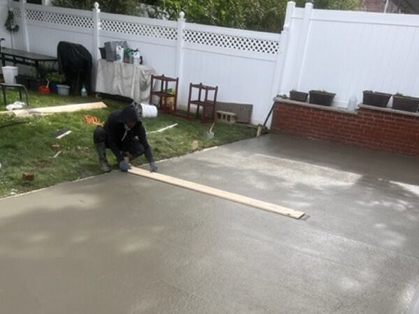 A man is working on a concrete driveway in a backyard.