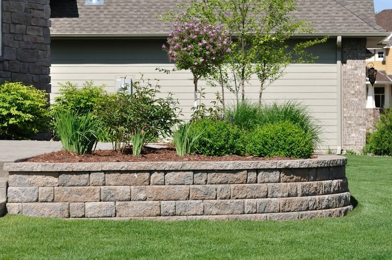 A brick wall with plants in it in front of a house