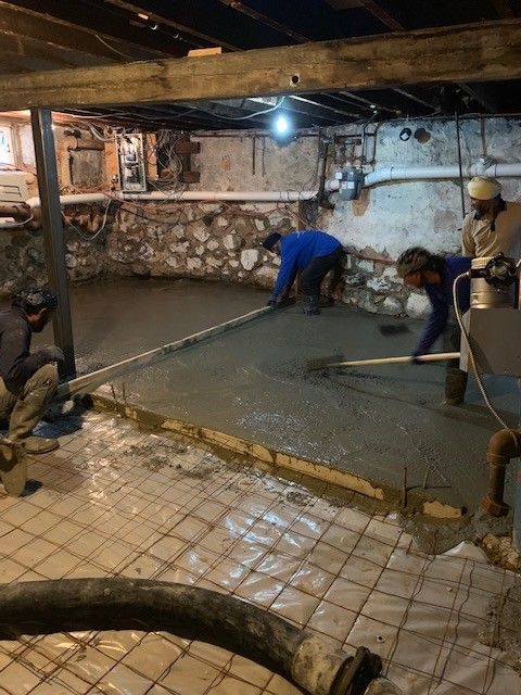 A group of men are working on a concrete floor in a basement.