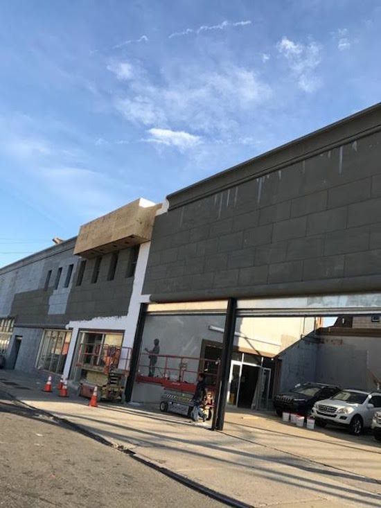 A large building under construction with cars parked in front of it.
