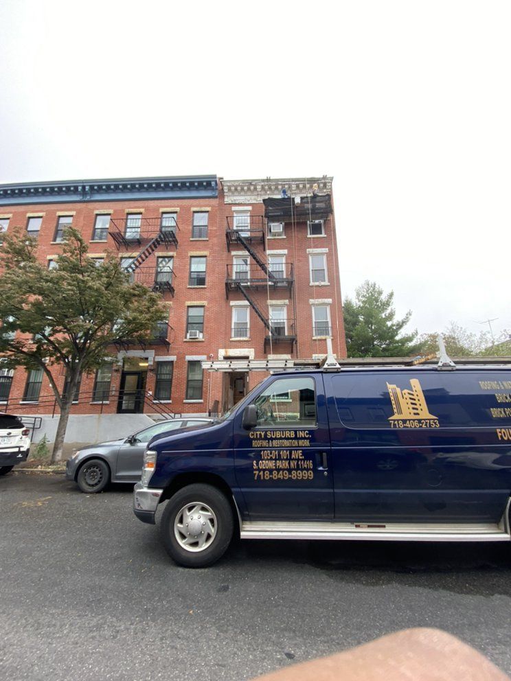 A blue van is parked in front of a brick building.