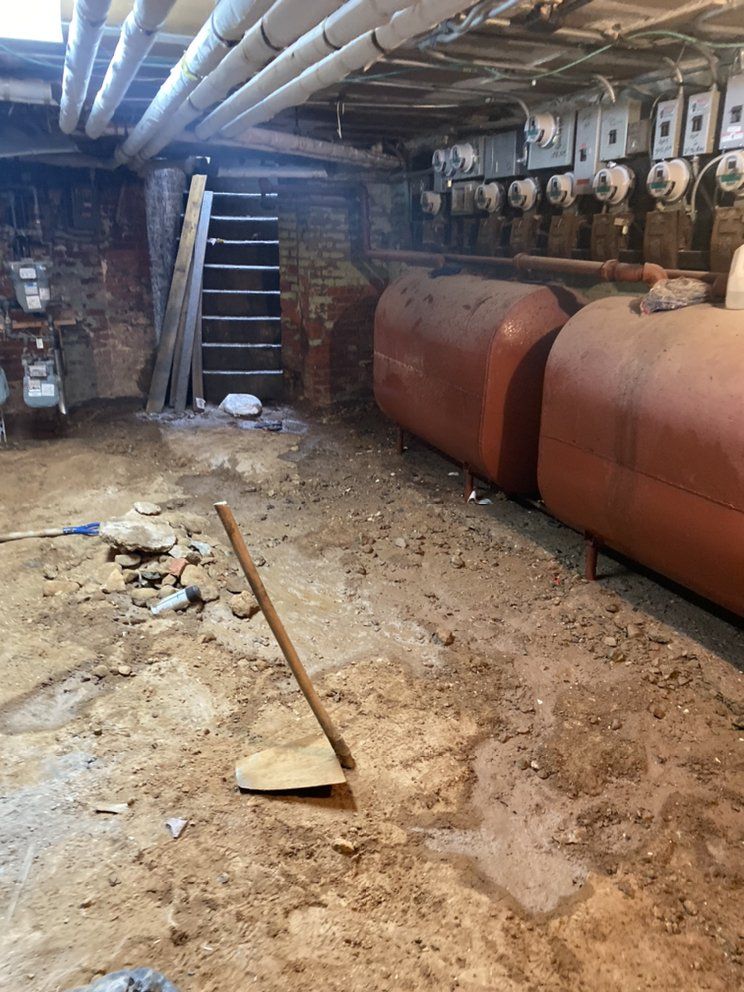 A dirty basement with a lot of pipes and tanks.