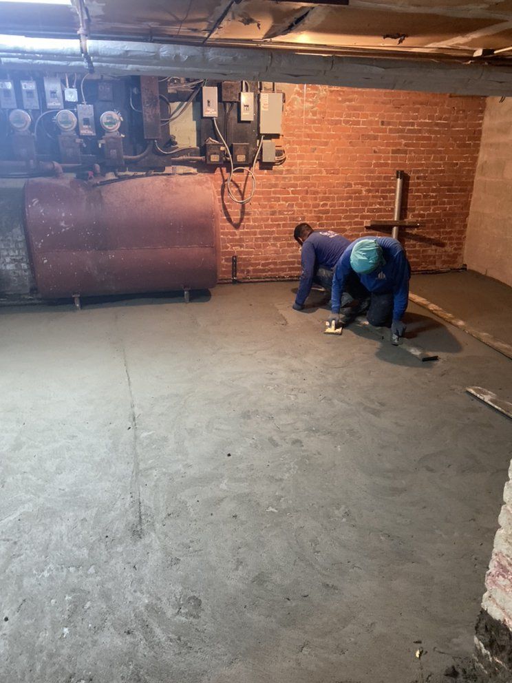 Two men are working on a concrete floor in a basement.