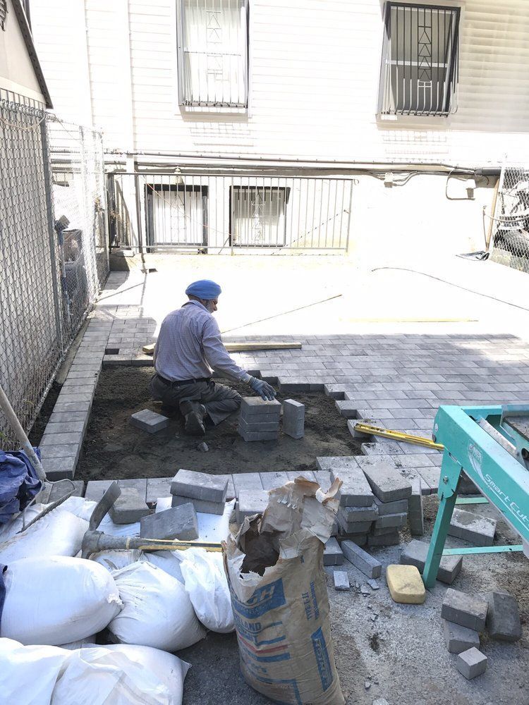 A man is laying bricks in a backyard in front of a building.