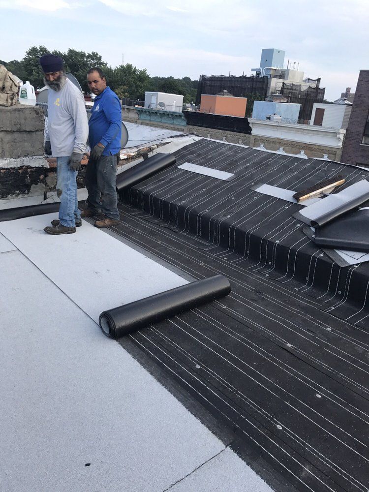 Two men standing on top of a roof with a roll of roofing material