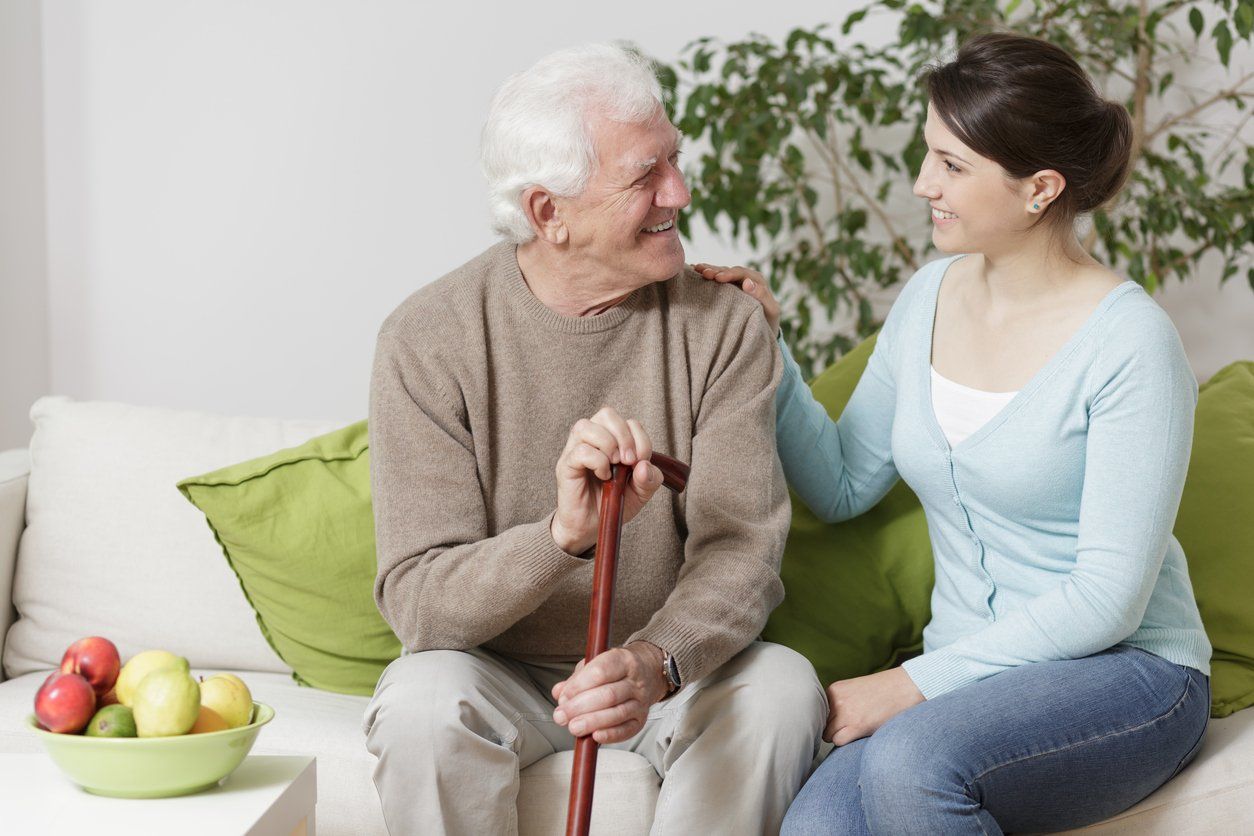 Elderly Male Holding Cane & Smiling at Young Woman While Sitting on Couch