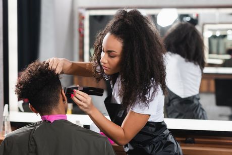 African american hairdresser in apron trimming head of client in salon